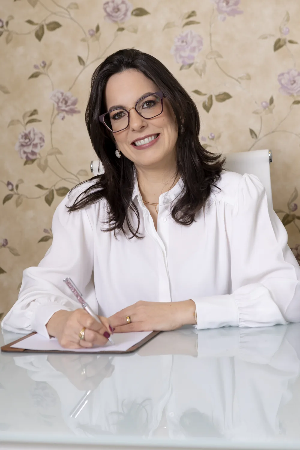 Dra. Thaisa Motta sentada à mesa, com uma caneta e um bloco de anotações.